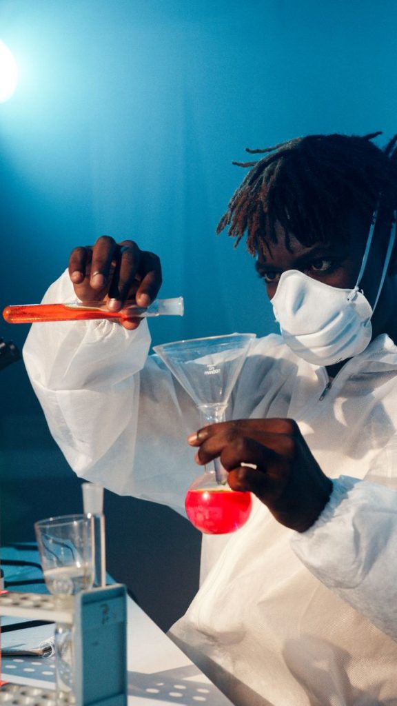 Scientist in protective gear carefully conducting a lab experiment with colorful liquids.